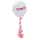 Un jouet en peluche en forme de ballon, avec des pois colorés et le mot "CÉLÉBRER" en lettres grasses, accompagné d'une corde tressée rose et blanche.