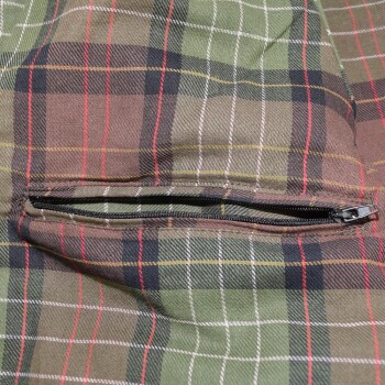 Nahaufnahme eines grün-braunen karierten Stoffes mit einer schwarzen Reißverschlusstasche, kein sichtbarer Text.