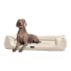 Ein brauner Hund sitzt auf einem plüschigen, cremefarbenen Hundebett. Der Text im Bild lautet 'INKLUSIVE' und 'MATRATZENSCHONER GIBT'S OBENDAUF.'