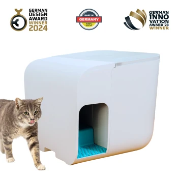 Eine graue getigerte Katze steht neben einer modernen weißen Katzentoilette mit blauem Innenraum, die Auszeichnungen für Design und Innovation zeigt.