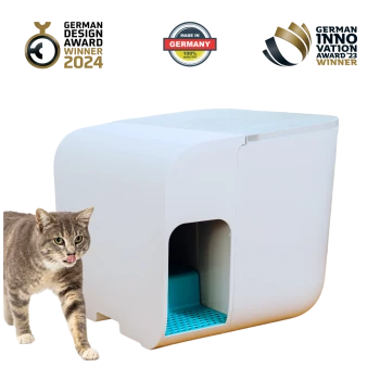 Eine graue getigerte Katze steht neben einer modernen weißen Katzentoilette mit blauem Innenraum, die Auszeichnungen für Design und Innovation zeigt.