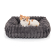 Kleiner weißer und brauner Chihuahua liegt in einem plüschigen, dunkelgrauen, gerippten Haustierbett auf weißem Hintergrund.