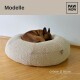 Ein brauner Hund, der sich auf einem runden, beigen Haustierbett mit strukturierter Oberfläche zusammenrollt, mit der Aufschrift 'Größe: Ø 80cm' und dem Markenlogo 'PAW WOW'.