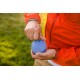 Eine Person in einer orangefarbenen Jacke hält einen blauen Haustier-Spielzeugball, bereit, ihn mit Leckereien zu füllen, vor einem grasbewachsenen Hintergrund.