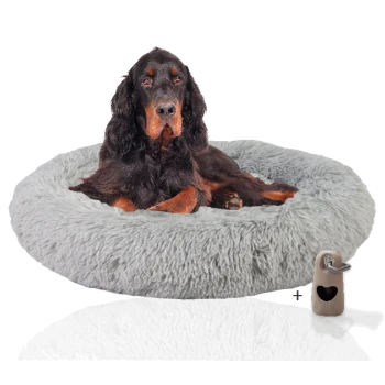 Ein schwarz-brauner Hund, der auf einem flauschigen grauen runden Hundebett ruht, mit einem kleinen beigen Spielzeug neben sich.