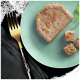 Eine Scheibe Haustierfutter-Pâté mit sichtbaren Gemüsestücken, serviert auf einem hellgrünen Teller, neben kleinen Würfeln des gleichen Pâtés und einer goldenen Gabel.
