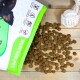 Eine teilweise geöffnete Lecker.Pet Hundefuttertüte, die braunes Futter auf einer Holzoberfläche auskippt, mit glutenfreien und zuckerfreien Symbolen.