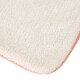 Eine Nahaufnahme einer weichen, flauschigen Haustiermatte in Cremefarbe mit einem rosa Rand, die ihre plüschige Textur und abgerundeten Kanten zeigt.