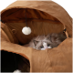 Blauäugige Ragdoll-Katze, die aus einem braunen kuppelförmigen Katzenbett hervorlugt; hängende weiße Bommelspielzeuge