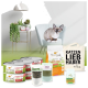 Eine Siamkatze sitzt auf einem blauen Stuhl in einem modernen Raum mit grünem Boden, umgeben von Tierfutterprodukten und einer Tragetasche.