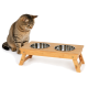 Getigerte Katze, die einen erhöhten Bambus-Futterspender mit zwei Edelstahlschalen vor weißem Hintergrund betrachtet.