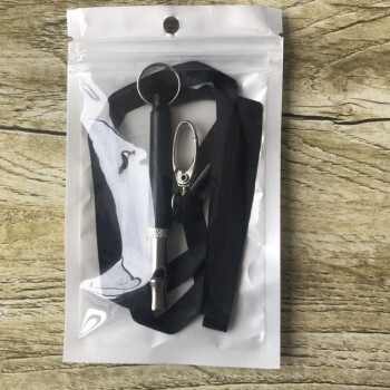 Ein schwarzer Klicker für die Haustierausbildung mit einem Lanyard, verpackt in einer klaren Plastiktüte, die auf einer Holzoberfläche ruht.