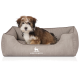 Flauschiger braun-weißer Welpe sitzt in einem grauen Hundebett mit weißem Hundelogo und dem Schriftzug 'KNUFFELWUFF'.