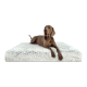 Ein entspannter brauner Hund liegt auf einem flauschigen weißen Haustierbett und schaut mit herausgestreckter Zunge zur Kamera.