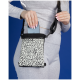 Eine Frau in einem grauen Outfit legt ein Smartphone in eine stilvolle schwarz-weiß gemusterte Umhängetasche vor einem blauen Hintergrund.