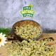 Eine Holzschüssel mit grünen Tierfutterflocken steht auf einer strukturierten Oberfläche, mit einigen verstreuten Flocken in der Nähe und einem "LYRA NATURE POWER" Logo darüber.
