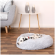 Ein gefleckter Dalmatiner-Welpe, der auf einem flauschigen grauen Haustierbett in einem gemütlichen Wohnzimmer ruht, mit einem grauen Sofa und dekorativen Vasen im Hintergrund.