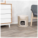 Ein gemütliches Katzenbett aus geflochtenem Material mit einer weichen Oberseite, mit einer grauen Katze, die aus dem Eingang schaut, neben einer modernen Kommode und einem Stuhl platziert.