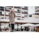 Eine Frau in einem Leopardenmuster-Mantel steht neben einem kleinen Hund, der eine passende Leopardenmuster-Jacke trägt, vor einem modernen urbanen Hintergrund.
