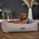 Ein brauner Hund ruht sich in einem gemütlichen, grauen Scruff's Hundebett aus, umgeben von dekorativen Pflanzen und einer modernen Vase in einem stilvollen Raum.
