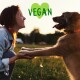 Eine Person und ein Hund interagieren auf einer grasbewachsenen Fläche während des Sonnenuntergangs. Der Text "VEGAN" wird deutlich in Grün über ihnen angezeigt.