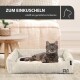 Eine gemütliche Katze entspannt sich in einem gerippten Haustierbett mit einem cremefarbenen Kissen, neben einem Holztisch und einer Pflanze. Text: "ZUM EINKUSCHELN."