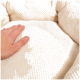 Eine Hand drückt sanft auf ein weiches, cremefarbenes Haustierbett mit einer strukturierten Oberfläche, das seinen plüschigen Komfort zeigt.