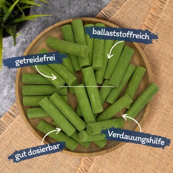 Holzschale mit grünen zylindrischen Pellet-Leckerchen, mit deutschen Etiketten: ‚getreidefrei‘, ‚ballaststoffreich‘, ‚gut dosierbar‘, ‚Verdauungshilfe‘.