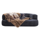 Ein großer grauer Hund und ein kleiner schwarzer Hund ruhen sich auf einer dunkelgrauen Couch aus, die mit einer braunen Decke bedeckt ist.