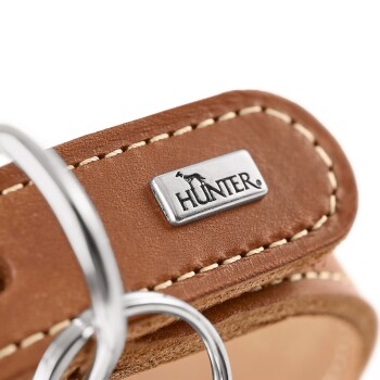 Nahaufnahme eines braun genähten Lederhalsbands mit Metallplakette „HUNTER“ und silbernen D-Ringen.
