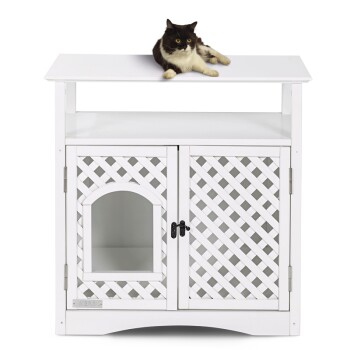 Czarny i biały kot wylegujący się na białym drewnianym domku dla zwierząt z kratkowymi drzwiami i łukowatym wejściem.