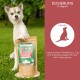Ein Hund steht im Freien neben einem Sack "Natural BARF Complete" Ergänzungspulver, mit Dosierungsanweisungen auf Deutsch an der Seite.