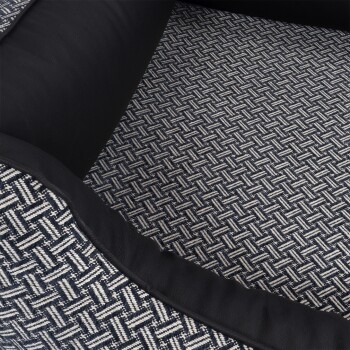 Eine Nahaufnahme eines Haustierbettes mit einem gewebten navyblauen und cremefarbenen Musterstoff mit schwarzem Lederbesatz.