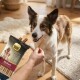 Chien de type border collie brun et blanc acceptant une friandise dentaire d'une main ; paquet de friandises Select Gold Sensitive Medium visible.