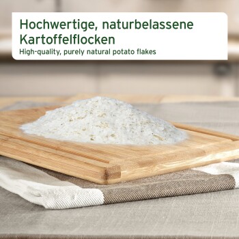 Weiße Kartoffelflocken auf einem Holzbrett auf Stoff; Etikett „Hochwertige, naturbelassene Kartoffelflocken“.