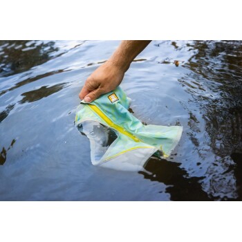 Eine Hand hält eine hellblaue und gelbe Hundeschwimmweste, die im Wasser eingetaucht ist, mit einem Logo, das einen Hund auf der Weste zeigt.