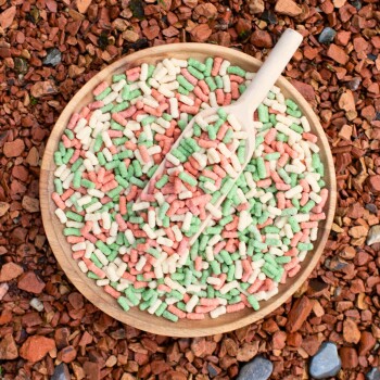 Bunte Fischfutterpellets in Grün, Orange und Gelb, verstreut auf Jute mit dem Text 'Lyra Pond - Alles für Ihren Teich.'