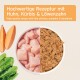 Hochwertiges Haustierfutter mit rohen Hühnerstücken, einer Schüssel mit braunem Haustierfutter und frischen Kürbis- und Löwenzahnblättern.