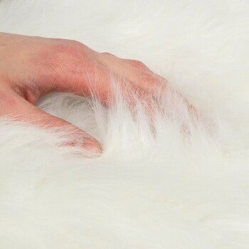 Eine Nahaufnahme einer Hand, die sanft weiches, flauschiges weißes Fell berührt, um die Textur und Weichheit des Materials zu zeigen.