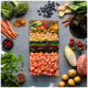 Ein buntes Arrangement aus frischem Gemüse und Lachs, darunter Brokkoli, Karotten, Süßkartoffeln und Heidelbeeren, auf einem grauen Hintergrund.