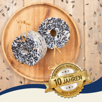 Zwei runde Vogelfutterkuchen mit Löchern, auf einem Holzbrett, umgeben von Sonnenblumenkernen und einem "Beste Qualität"-Abzeichen.