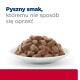 Biała talerz wypełniony wilgotnymi, brązowymi granulkami karmy dla zwierząt, towarzyszy mu tekst "Pyszny smak, któremu nie sposób się oprzeć" w pogrubionej i regularnej czcionce.