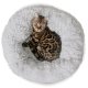Eine Bengal-Katze mit grünen Augen ruht sich bequem in einem flauschigen, runden, weißen Haustierbett aus.