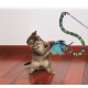 Ein verspieltes graues Tabby-Kätzchen, das nach einem bunten Feder-Spielzeug greift, das an einem langen, gemusterten Stock auf einem Holzboden befestigt ist.