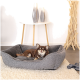 Ein entspannter brauner Chihuahua liegt in einem gemütlichen grauen Haustierbett auf einem weichen Teppich, mit einem modernen Tisch und dekorativen Vasen im Hintergrund.