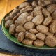 Eine Nahaufnahme eines grünen Tellers, gefüllt mit braunen, ovalen Haustierfutterkroketten, auf einer schwarzen Schieferoberfläche.