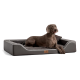 Ein brauner Hund entspannt sich auf einem stilvollen grauen Haustierbett mit einem plüschigen Innenraum und einem Holzschild mit der Aufschrift "Snoozer."
