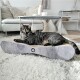 Eine elegante schwarze getigerte Katze liegt auf einem modernen, geschwungenen Kratzpad mit einem Logo, in einem gemütlichen Wohnzimmer mit einem hellen Teppich und Möbeln.