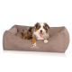 Ein glücklicher Australian Shepherd Hund, der in einem gemütlichen braunen Hundebett mit dem Logo "KNUFFELWUFF" auf der Vorderseite entspannt.