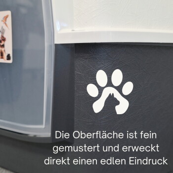 Nahaufnahme eines dunkel strukturierten Panels einer Transportbox mit weißem Pfotenlogo und deutschem Text: 'Die Oberfläche ist fein gemustert...'.